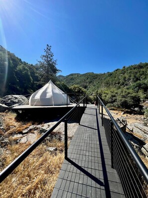 A white tent-like structure with a metal staircase leading up to it, surrounded by rocky terrain and greenery.