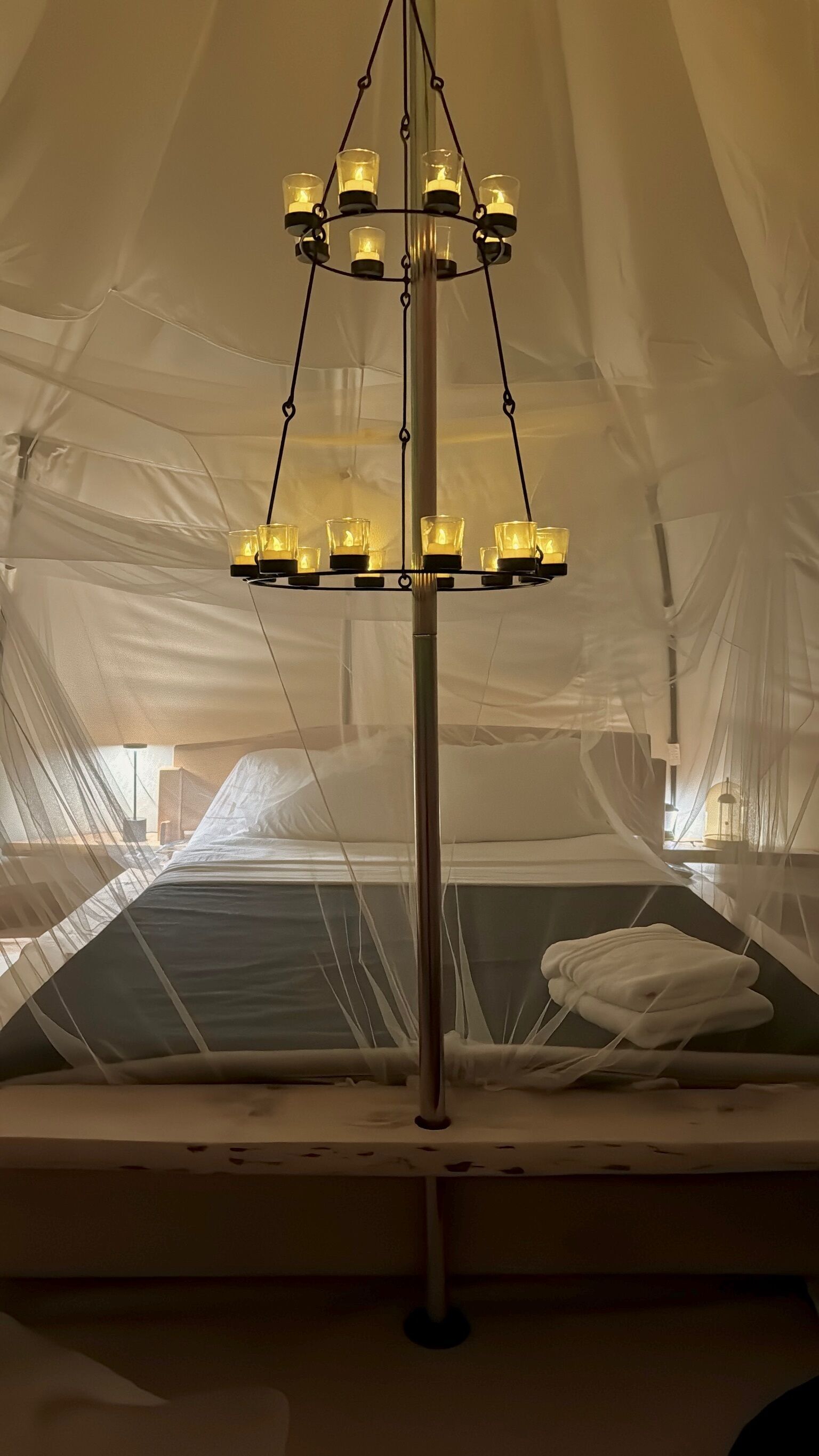 A tent with a hanging light fixture and a bed with a white blanket.