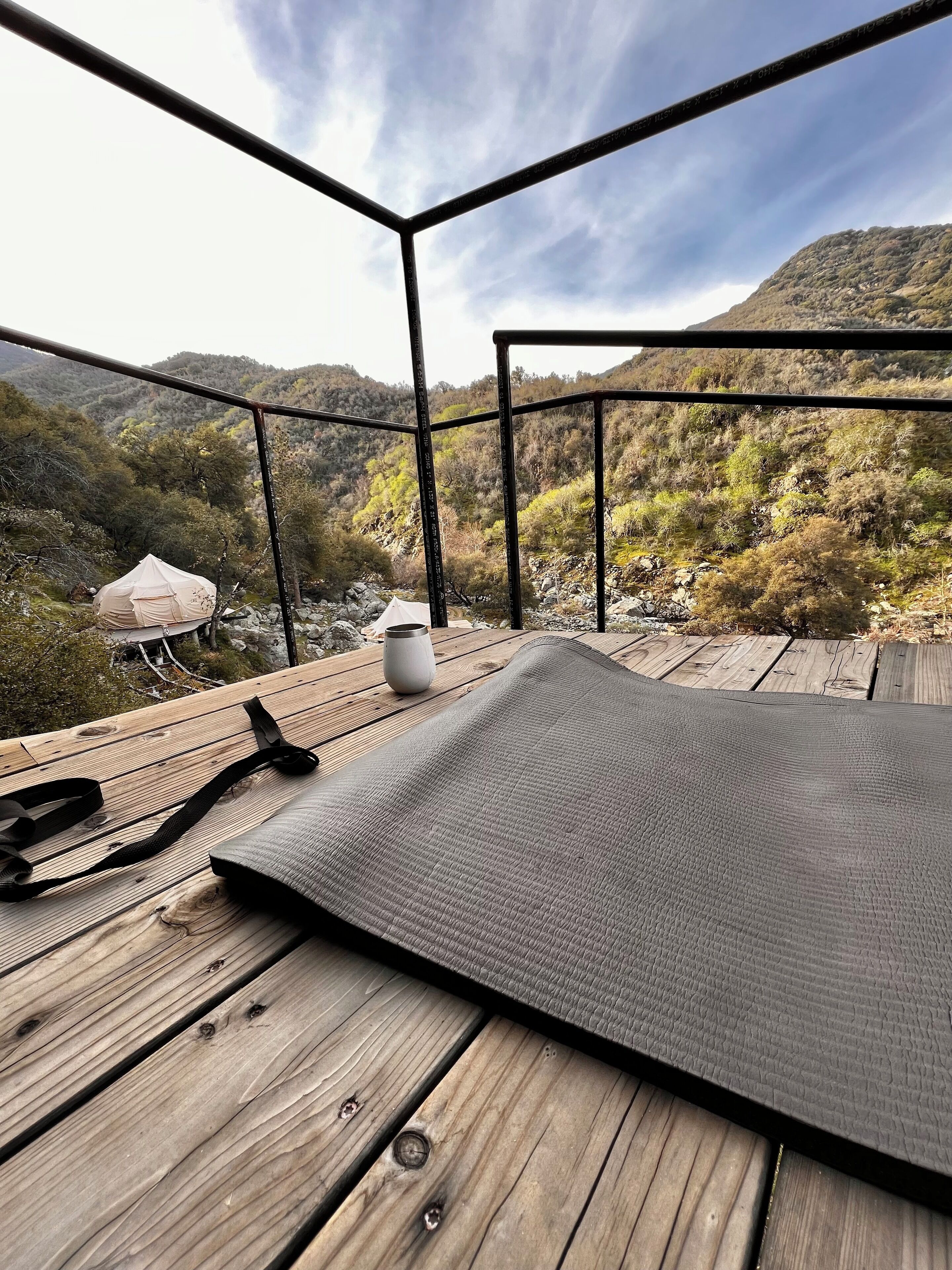 Eine Holzterrasse mit Yogamatte, Wasserflasche und Zelt im Hintergrund.
