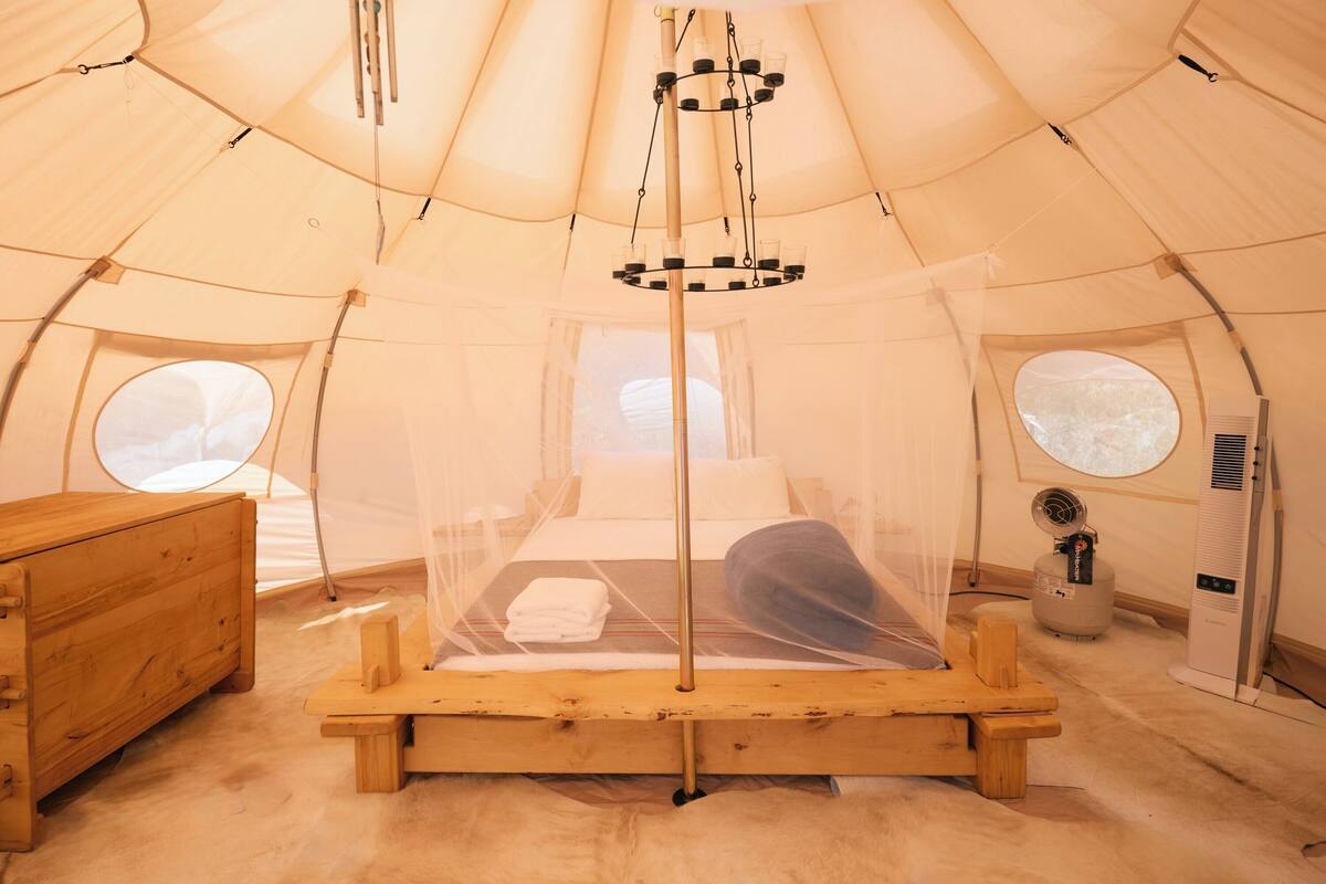 A tent with a bed, a wooden dresser, a heater, and a window.