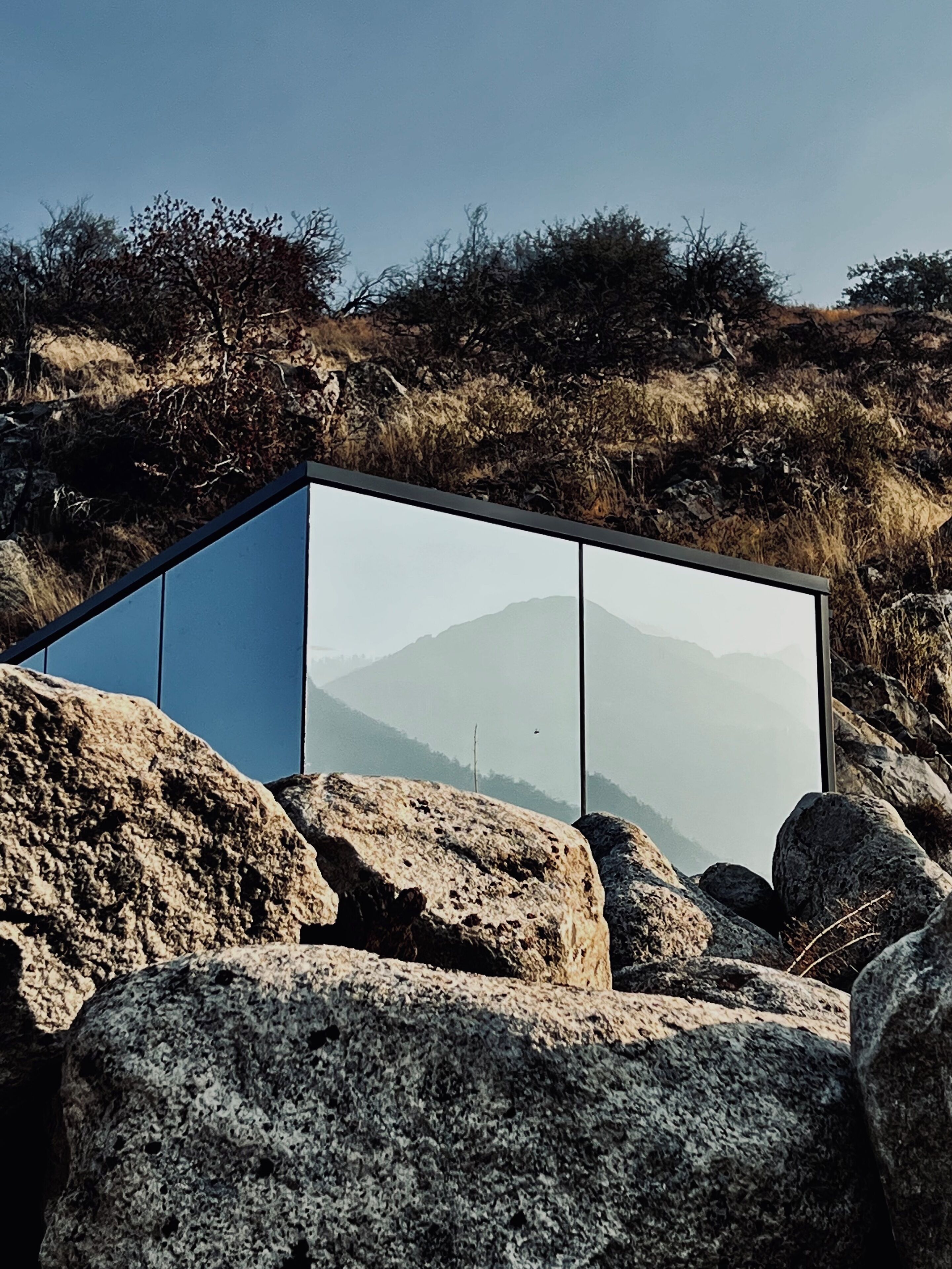 Une structure moderne et minimaliste, dotée d’une façade en verre, située sur un terrain rocheux avec une chaîne de montagnes en arrière-plan.