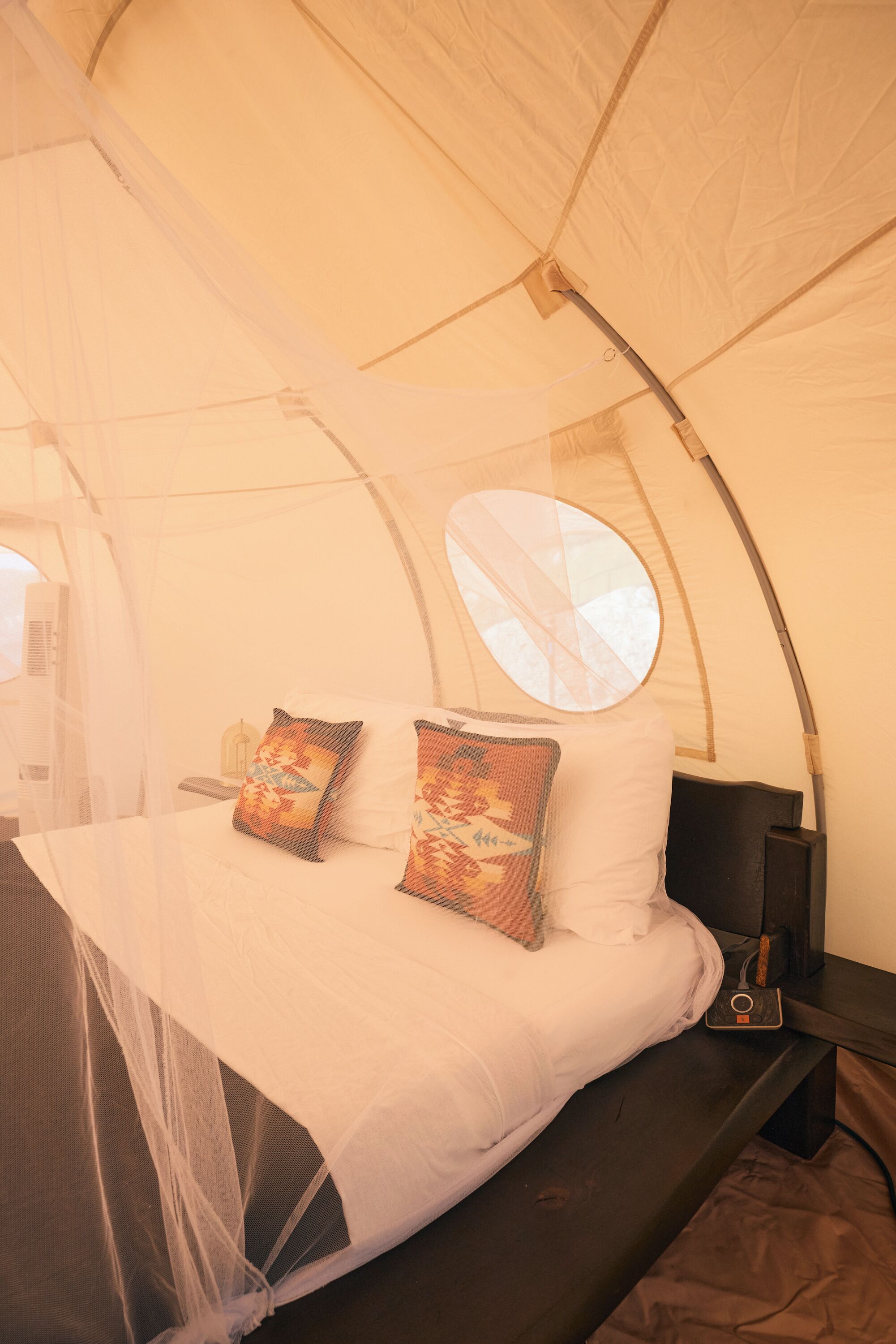 A tent with a bed, pillows, a nightstand, and a lamp.