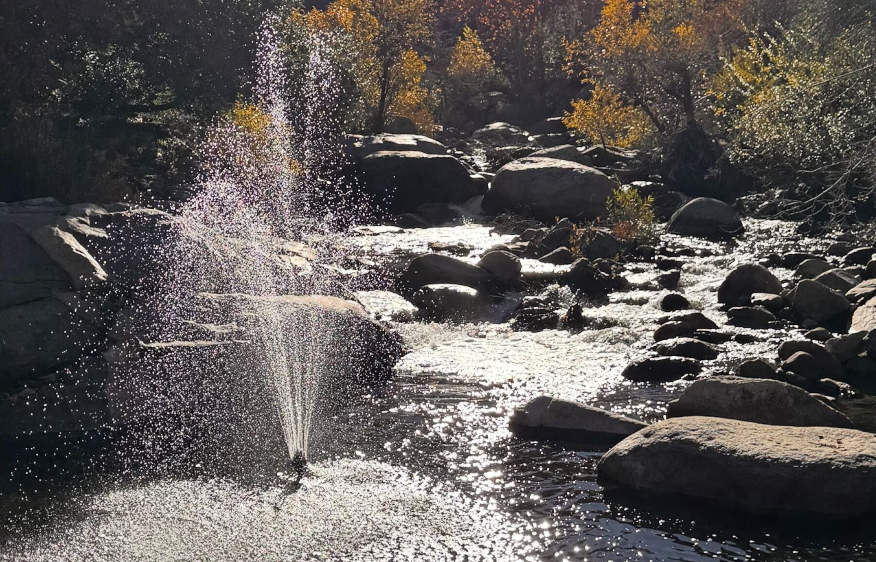 A waterfall in a rocky terrain with autumn foliage in the background.