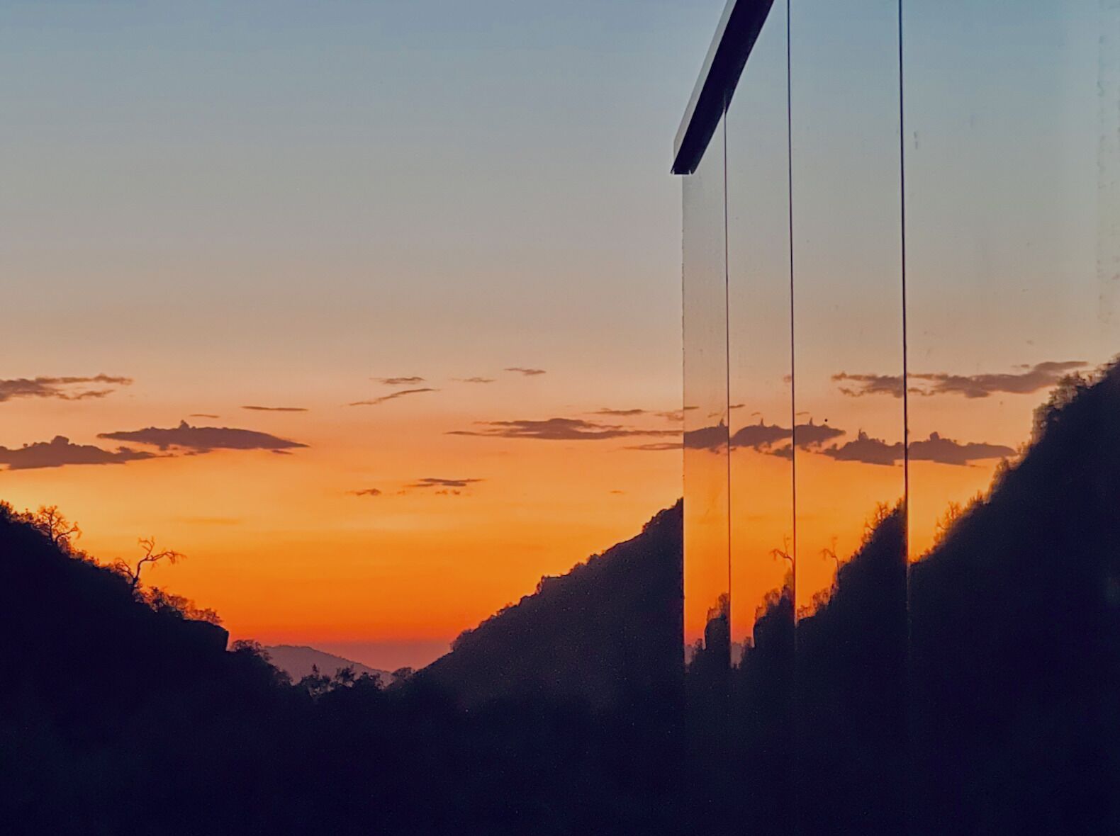 A sunset view from a window with a view of a valley and distant mountains.
