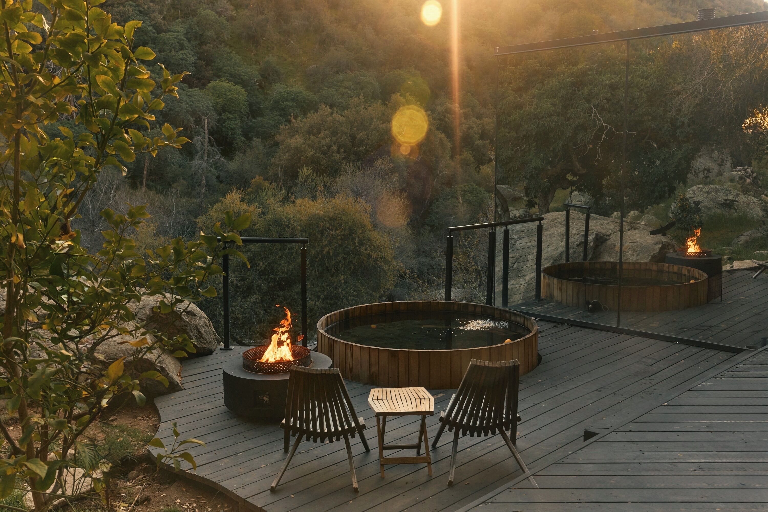 A wooden deck with a hot tub, two chairs, and a fire pit.