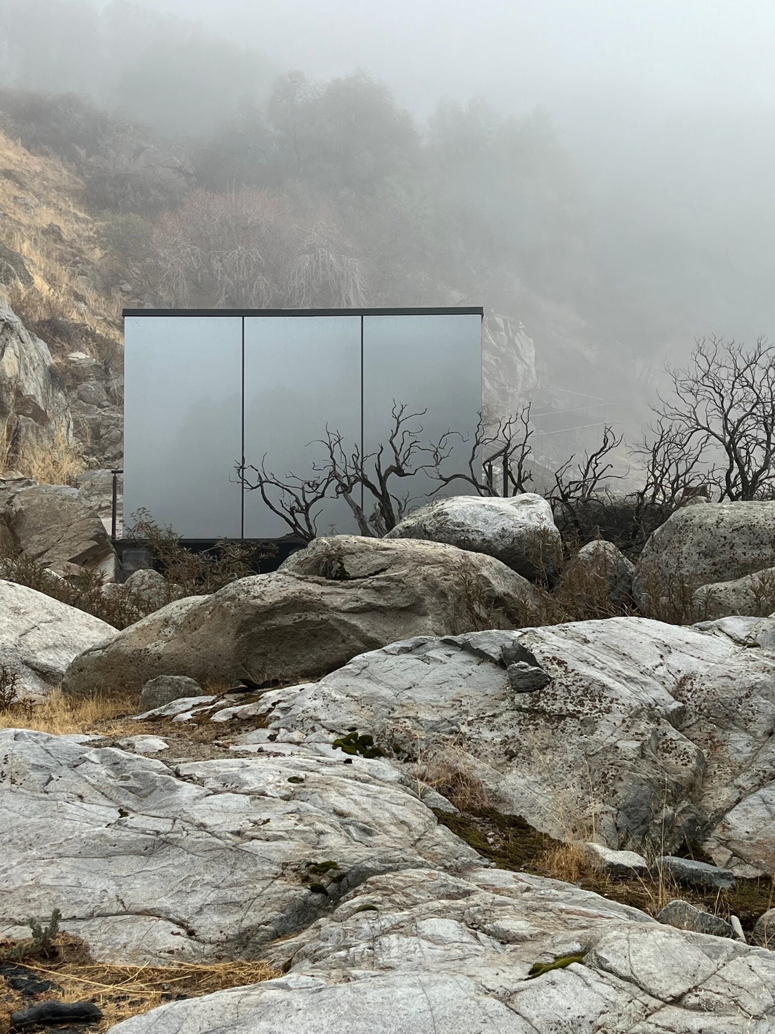 A modern building with a minimalist design, situated in a rocky landscape with sparse vegetation.