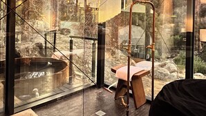 Un bagno moderno con cabina doccia in vetro, una panca in legno e vista su un paesaggio montuoso.