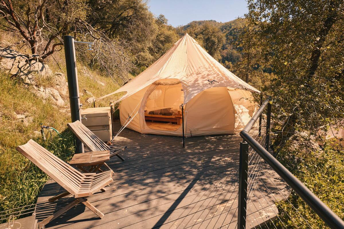 A tent with a wooden deck, a bench, and a metal railing.