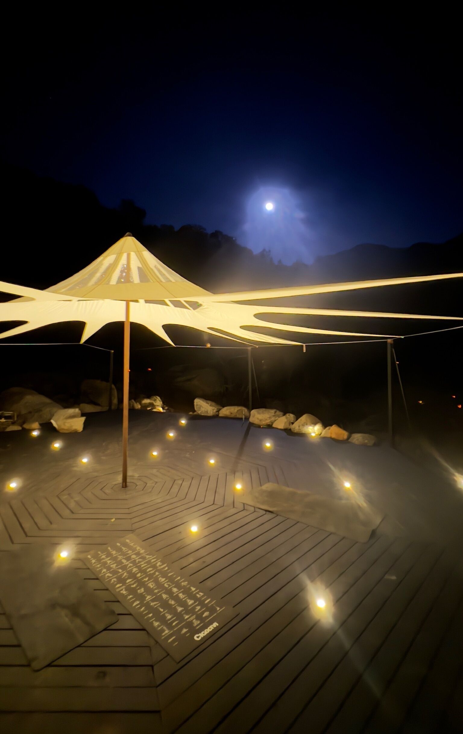 A wooden deck with a canopy structure, illuminated by ambient lighting.