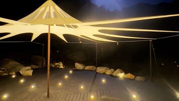 Una terraza de madera con estructura cubierta, iluminada por luces ambientales.