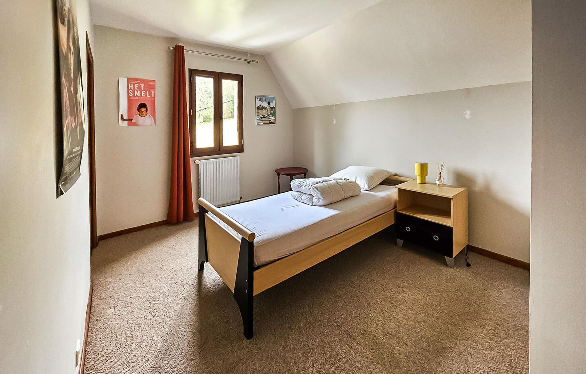 A bedroom with a single bed, a nightstand, a small table, and a radiator.