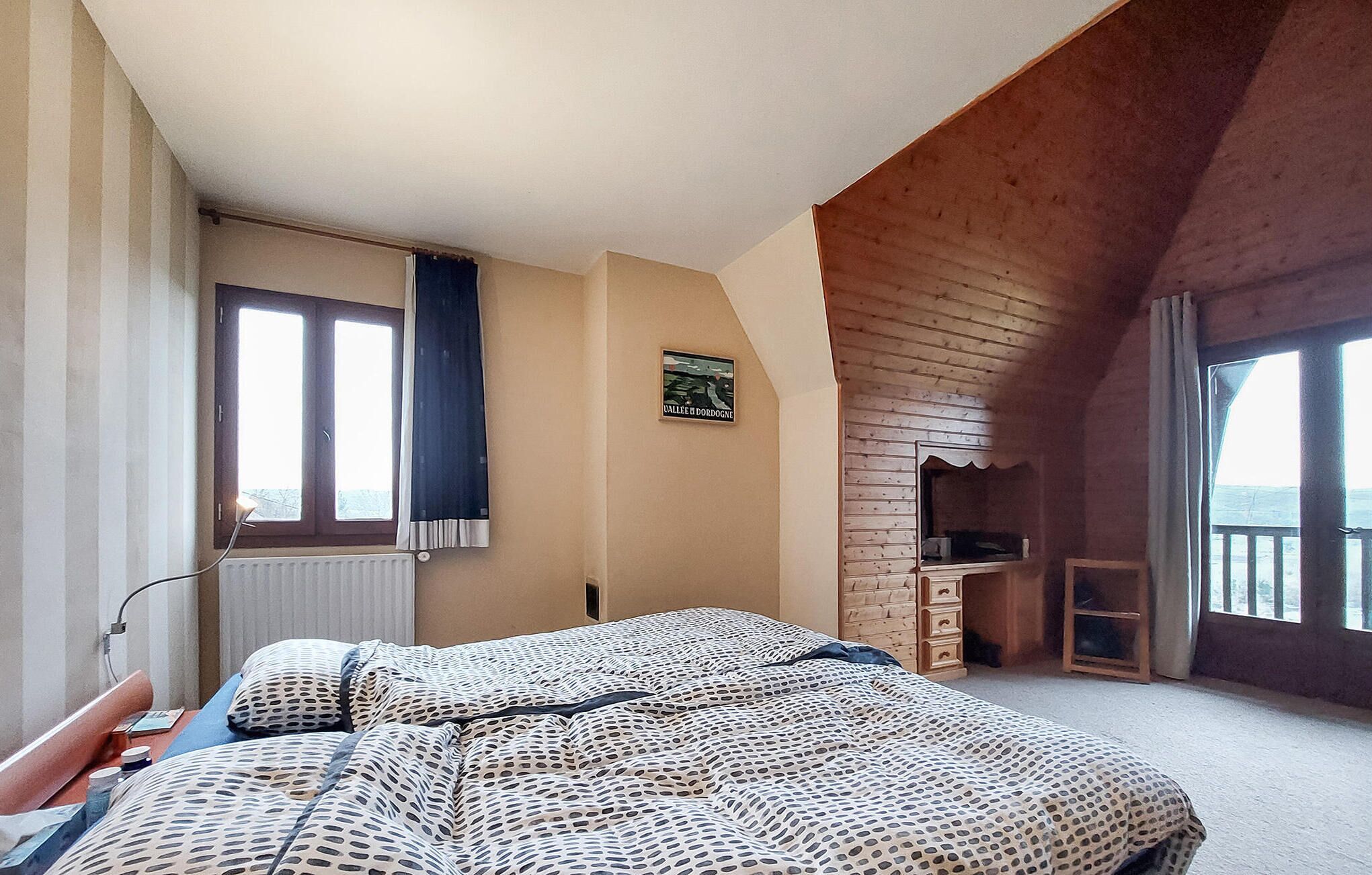 Een slaapkamer met een bed, een raam, een radiator, een houten plafond en een klein bureau.