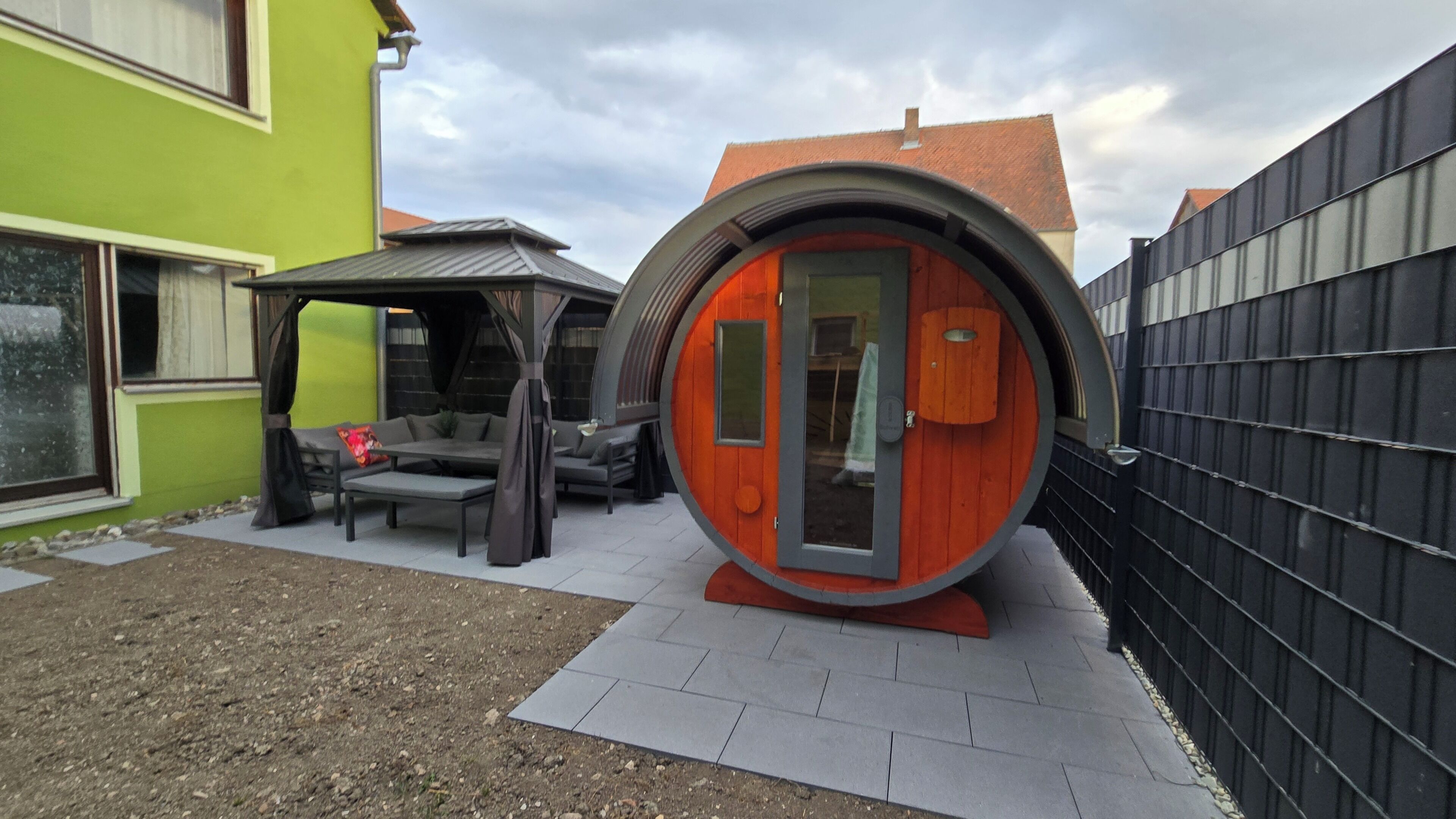A modern house with a unique circular structure, a green exterior wall, and a patio area with outdoor furniture.