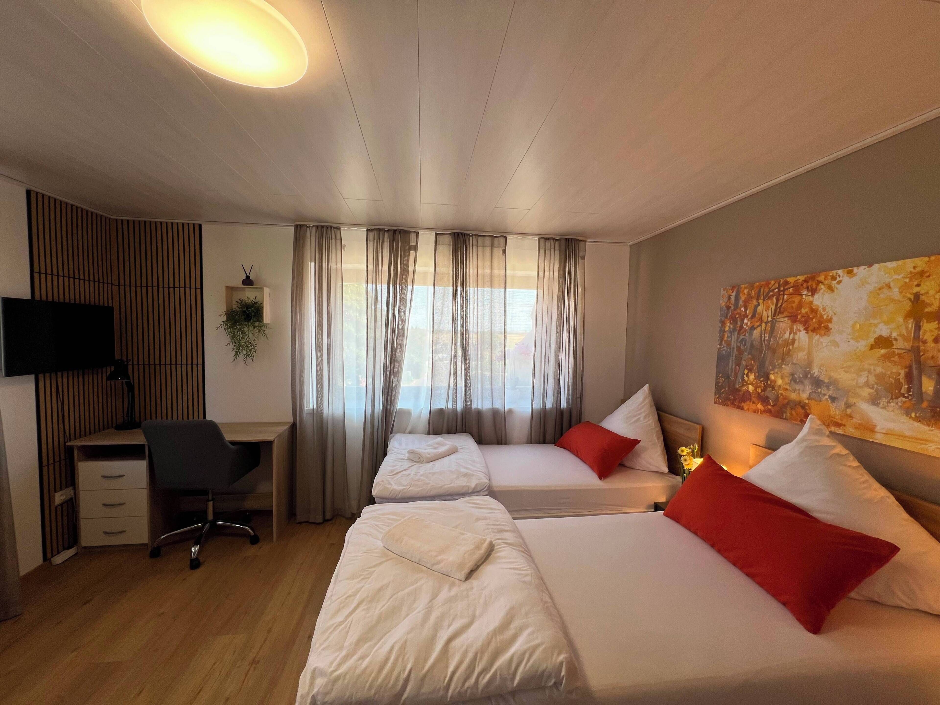 A hotel room with two beds, a desk, a chair, a TV, and a painting on the wall.
