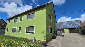 Ein zweistöckiges Gebäude mit grüner Fassade, zahlreichen Fenstern und einer Solaranlage auf dem Dach.
