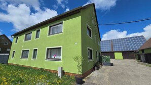 Un edificio de dos pisos con fachada verde, varias ventanas y un conjunto de paneles solares en el techo.