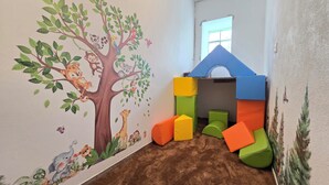Un cuarto de juegos infantil con un mural de un árbol, bloques de juego coloridos y una ventana.