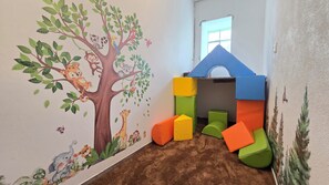 Ein Kinderzimmer mit einer Baummalerei, bunten Spielklötzen und einem Fenster.