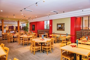 Ein geräumiges Restaurant mit mehreren Holztischen und -stühlen, einer roten Akzentwand und einem großen Fenster, das für natürliches Licht sorgt.
