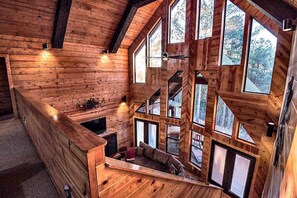 A log cabin interior with a loft bedroom, large windows, and a fireplace. - Stairway to Heaven | 7BR Luxury | Pickle Ball | Mountain views (Broken Bow)