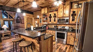 Une cuisine rustique avec des meubles en bois, un îlot central doté de tabourets, des appareils électroménagers en acier inoxydable et des luminaires suspendus.