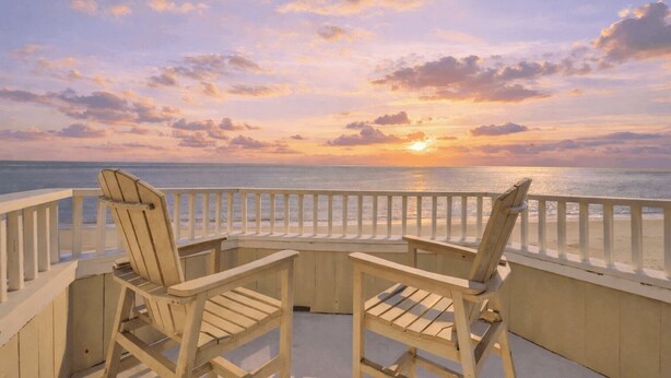 Une terrasse en bois avec deux fauteuils Adirondack donnant sur un coucher de soleil sur l’océan.