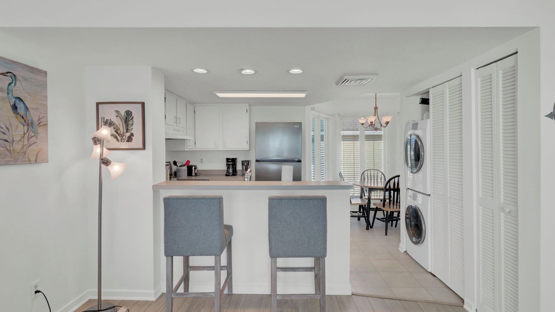 A modern kitchen with white cabinets, a stainless steel refrigerator, and a bar area with two grey barstools.