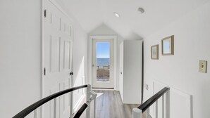 Un couloir avec des portes blanches, une vue sur l’extérieur et un escalier avec des rampes noires.