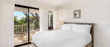 Un dormitorio con una cama grande, un balcón y vistas a árboles.