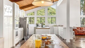 Una cocina amplia con armarios blancos, una mesa de comedor de madera y ventanas grandes con vistas a zonas verdes.