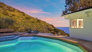 Una piscina con vista al océano, un banco y una casa con un gran ventanal.