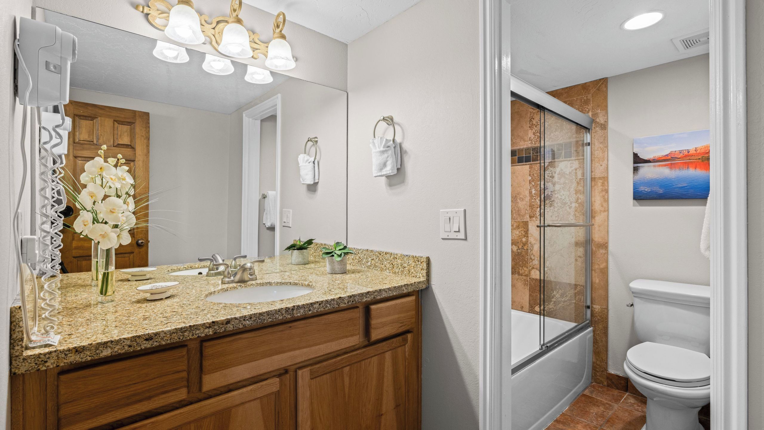 A bathroom with a granite countertop, two sinks, a mirror, a shower with glass doors, and a toilet.
