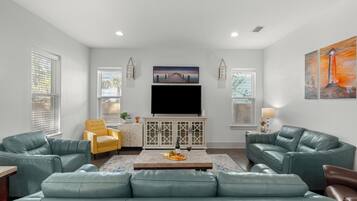A living room with a flat-screen TV, two sofas, a coffee table with snacks, and a painting on the wall.