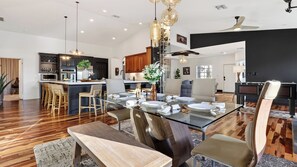 A modern kitchen with a central island, dining area with a glass table, and a living space with a dark accent wall.