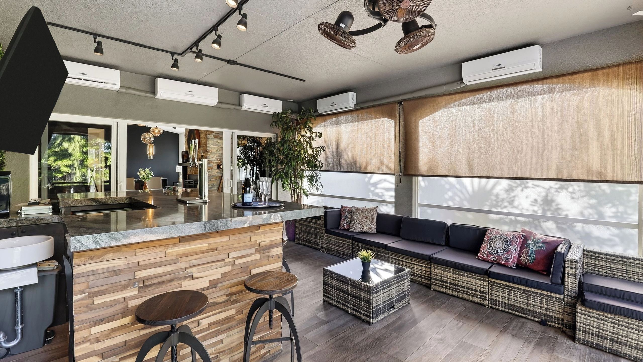 A modern kitchen with a central island, bar stools, a seating area with a sofa and cushions, and a large window with a view.