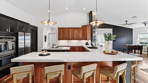 A modern kitchen with a large island, wooden cabinets, stainless steel appliances, and pendant lighting.