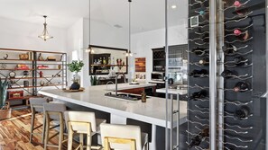 A modern kitchen with a central island, bar stools, wine rack, and various kitchen appliances.