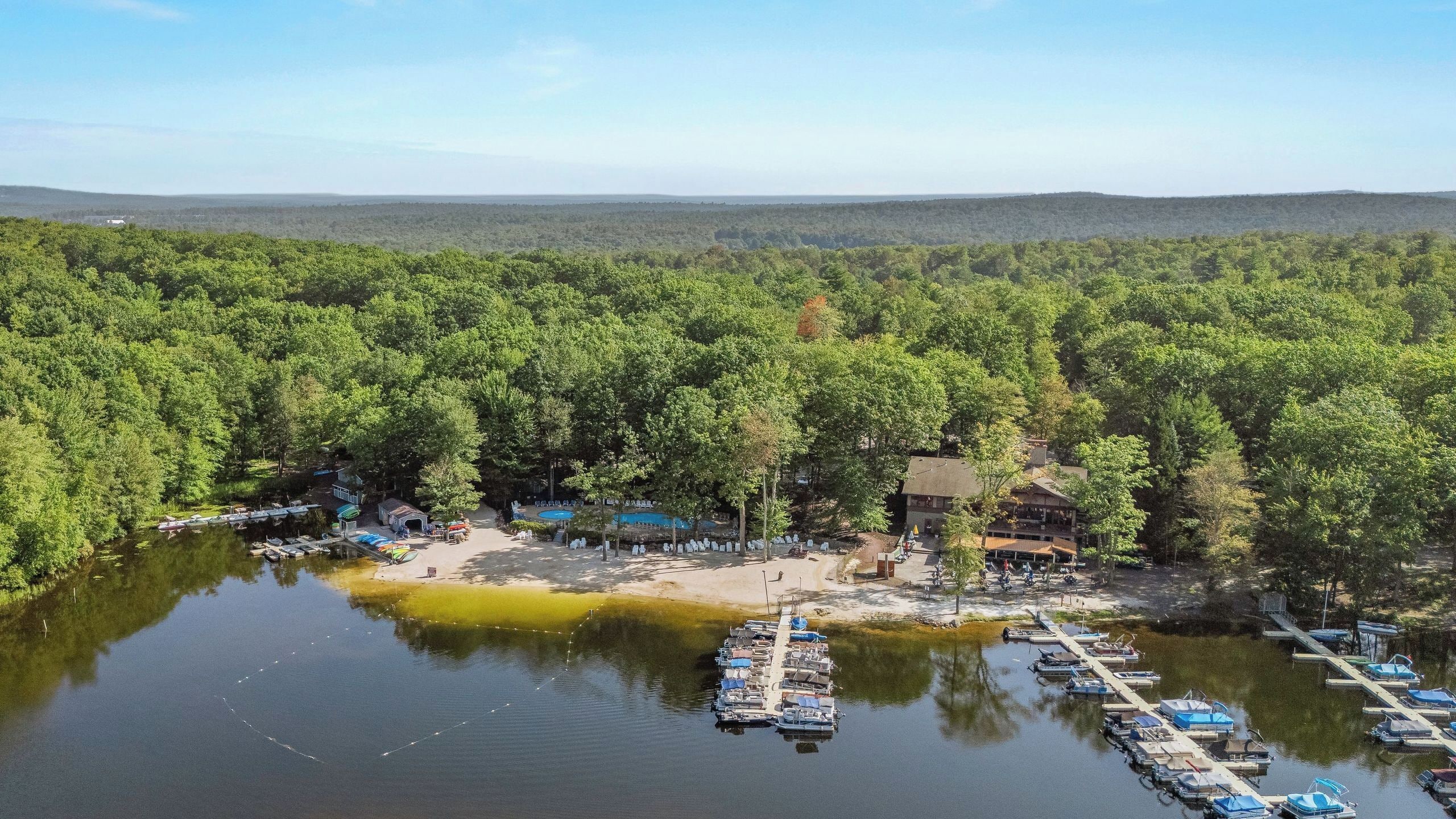 A lakeside property with a dock, boats, and a building surrounded by dense forest.