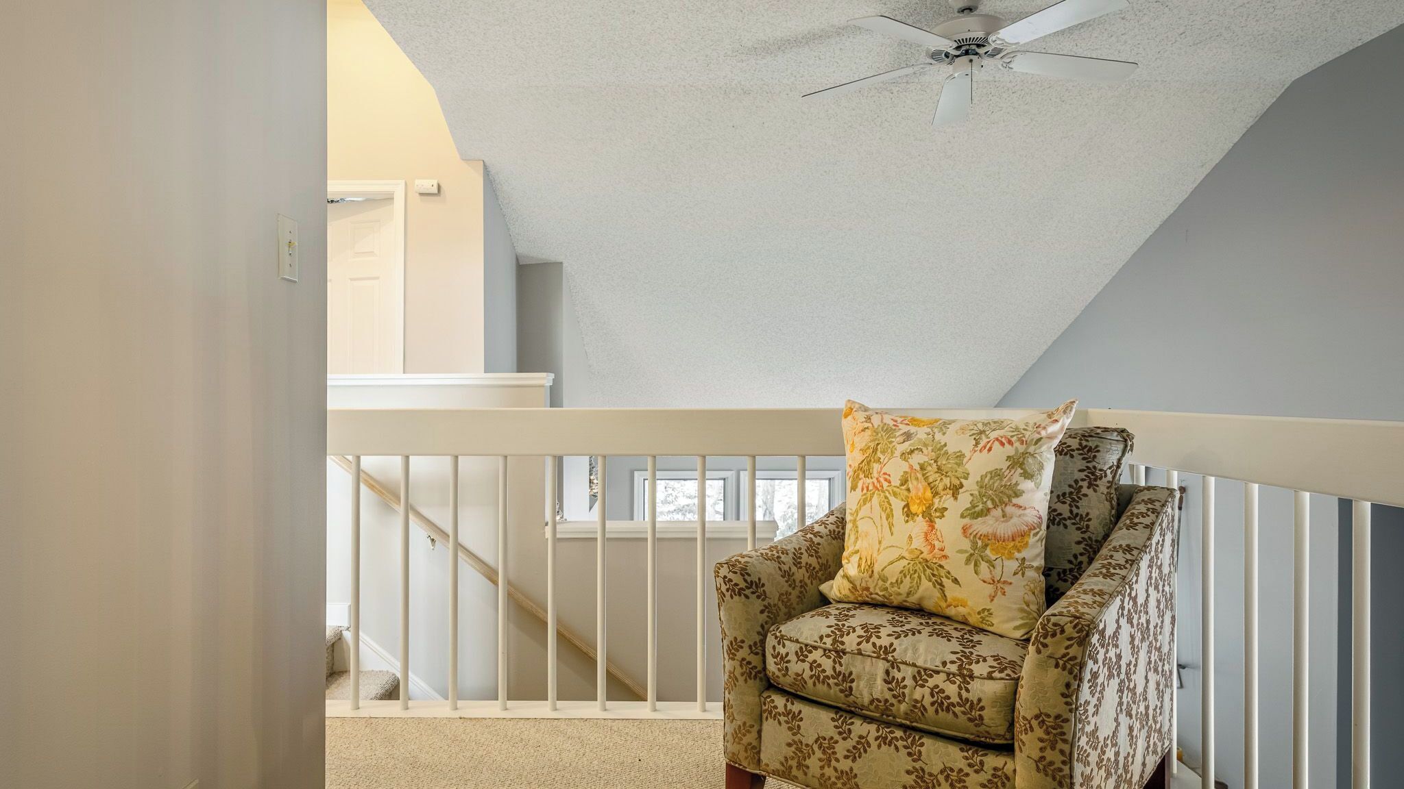 Une pièce avec une rambarde blanche, un ventilateur de plafond et un fauteuil à motifs floraux.