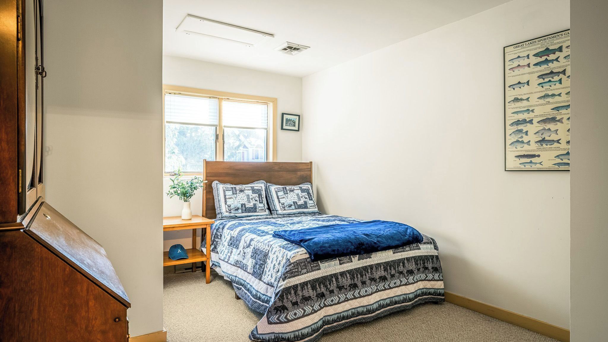 A bedroom with a bed, a nightstand, a window, and a wall-mounted fish chart.