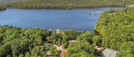 Um lago rodeado por floresta densa, uma quadra de tênis e um pequeno edifício.