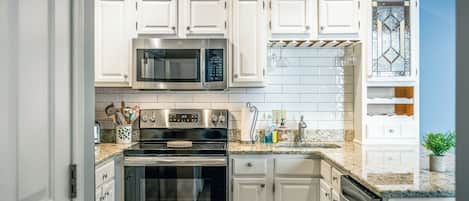 A kitchen with white cabinets, a stainless steel microwave, an oven, and a granite countertop.