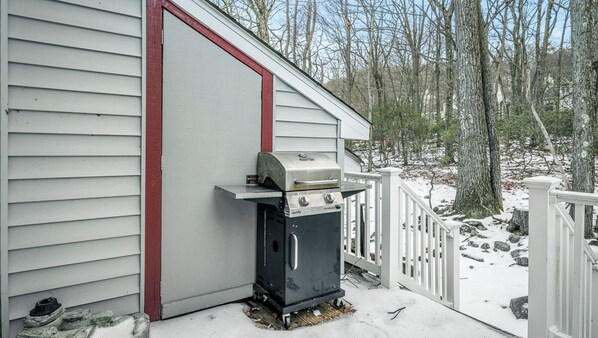 A portable grill outside a house with a white exterior and red trim, set in a snowy forest. - Mountain Laurel Lodge by Avantstay Lake Harmony Retreat Loft + Games + Ski + Private Club Access (Lake Harmony)