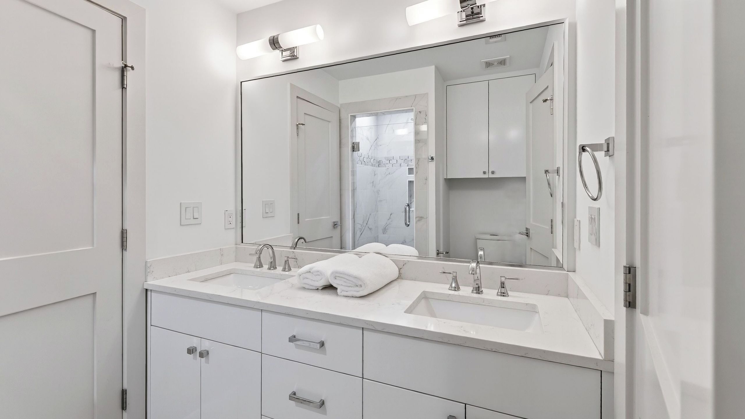 A modern bathroom with a large mirror, two sinks, and a walk-in shower.