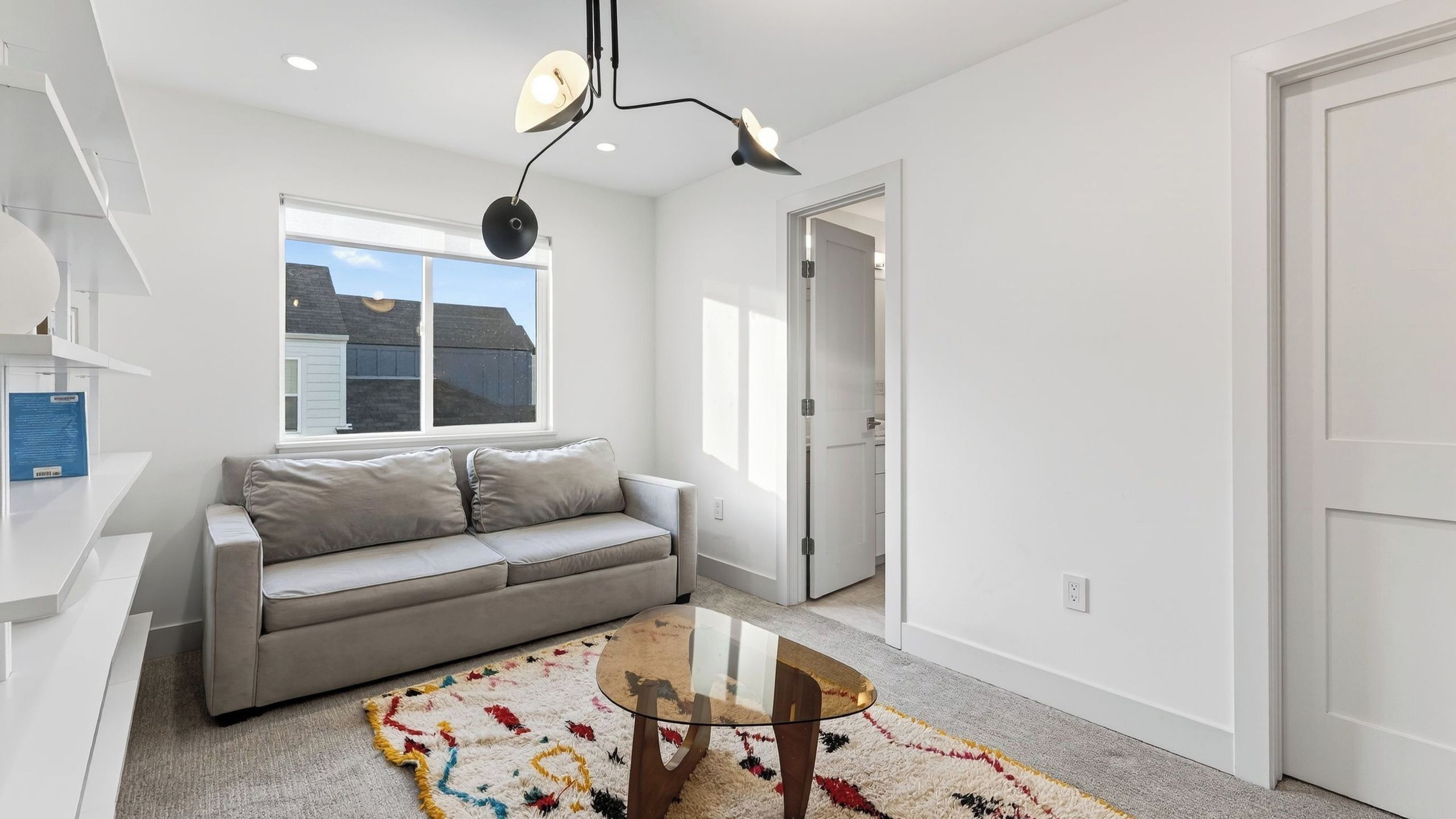 Een moderne woonkamer met een grijze bank, een glazen salontafel en een kleurrijk vloerkleed.