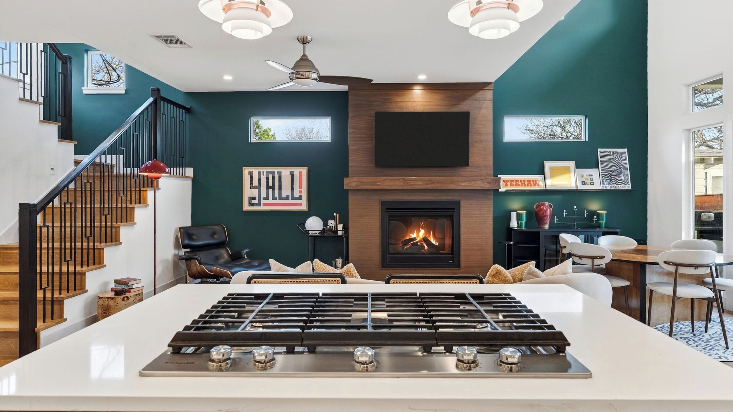 Un salon moderne avec une cheminée, un îlot de cuisine doté d’une cuisinière à gaz, un escalier et un coin repas.