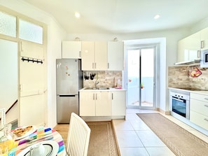 A modern kitchen with white cabinets, stainless steel appliances, and a dining area with a colorful tablecloth. - Laila Summer Escape by GT House (Portimão)