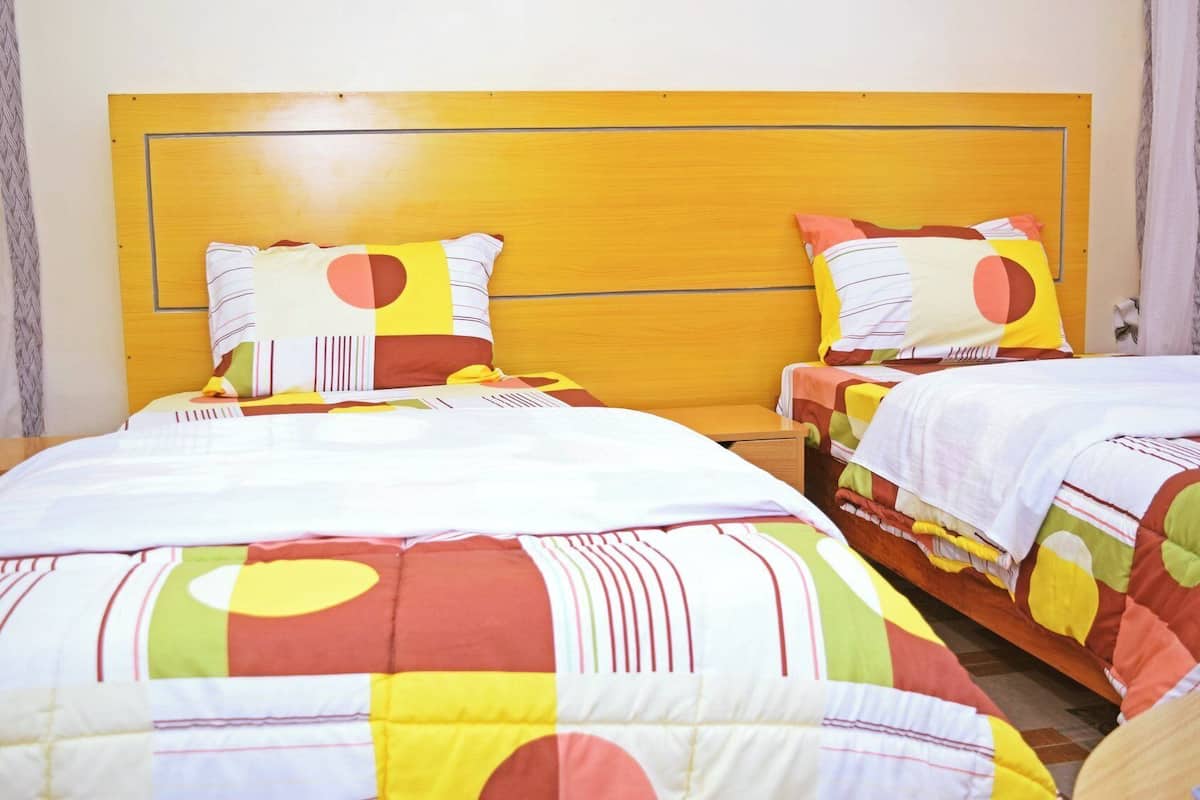 A hotel room with two beds, each with a wooden headboard and colorful bedding.