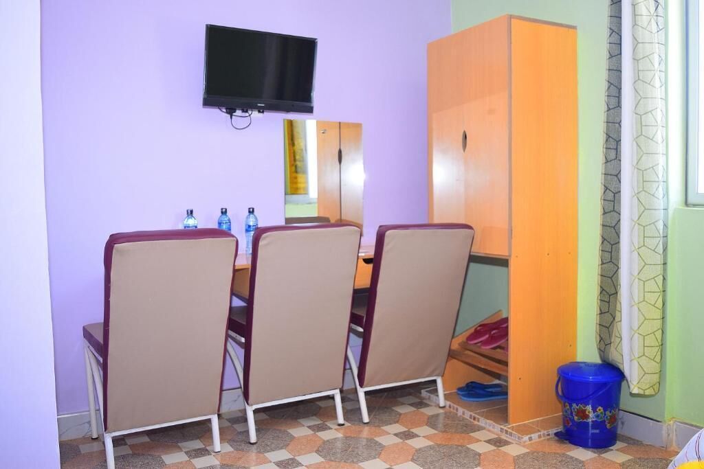 A room with a television mounted on the wall, a wooden wardrobe, and a checkered floor.