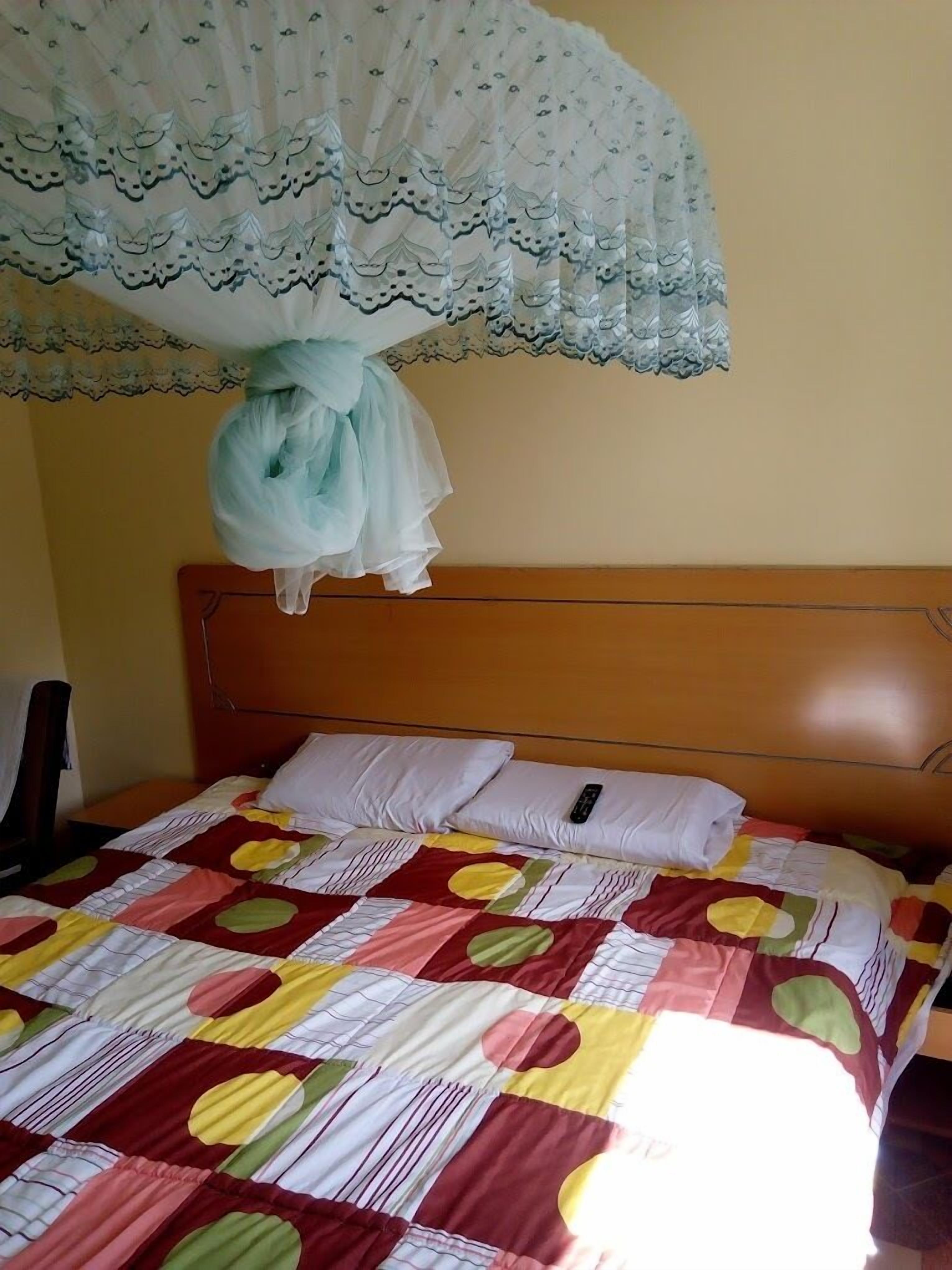 A bed with a colorful quilt, a white pillow, and a remote control on it.